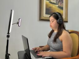 Luísa Camargos, mulher brnca, jovem e com Síndrome de Dwon, trabalha como RP em frente a computador