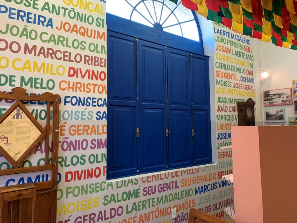 Parede da Estação de Memórias de Matozinhos, com nomes coloridos pintados em torno de janela de madeira azul.